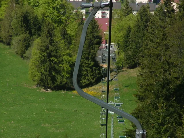 Kurvige Seilbahntrasse durch eine grüne Waldlandschaft mit Sesselliften