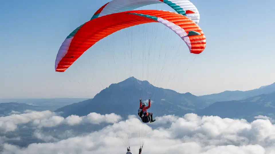 Zwei bunte Paragleiter gleiten über Wolken vor Bergkette