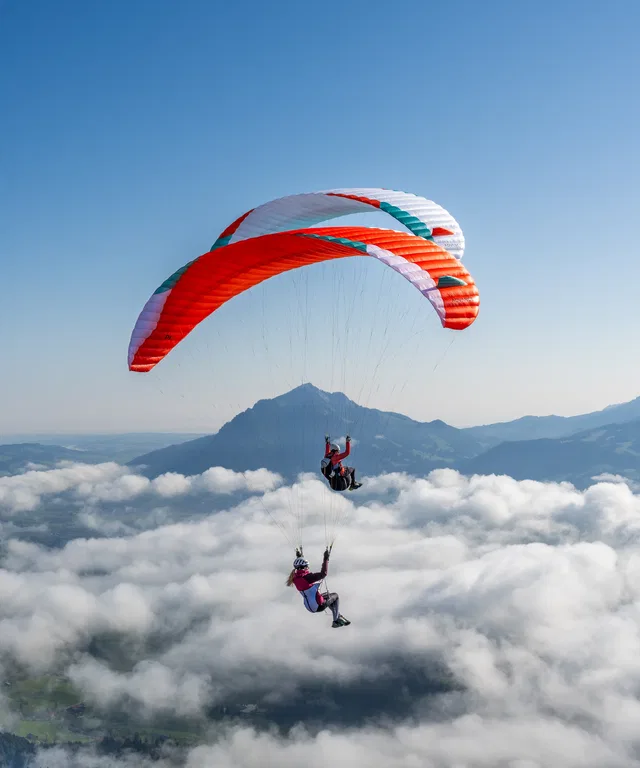 Zwei bunte Paragleiter gleiten über Wolken vor Bergkette