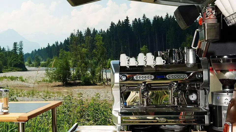 Große Espressomaschine in einem mobilen Barista-Anhänger im Grünen, Tassen bereit auf dem Wagen.