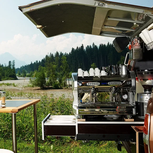 Große Espressomaschine in einem mobilen Barista-Anhänger im Grünen, Tassen bereit auf dem Wagen.