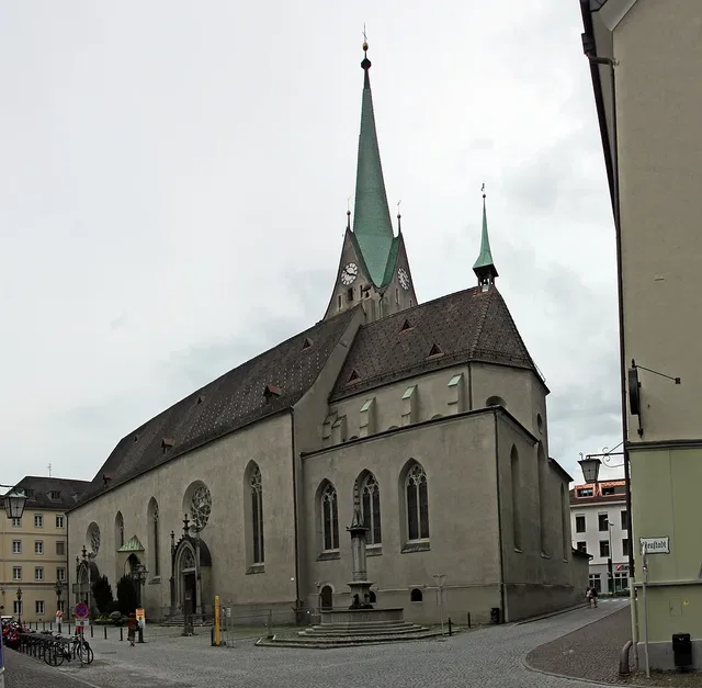Historische Kirche mit hoch aufragenden, grün patinierten Türmen aus Stein vor einer Platz- und Stra