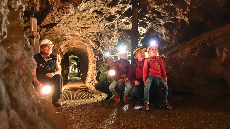 Besucher mit Helmen und Lampen im historischen Erzstollen