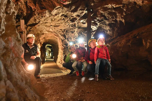 Besucher mit Helmen und Lampen im historischen Erzstollen