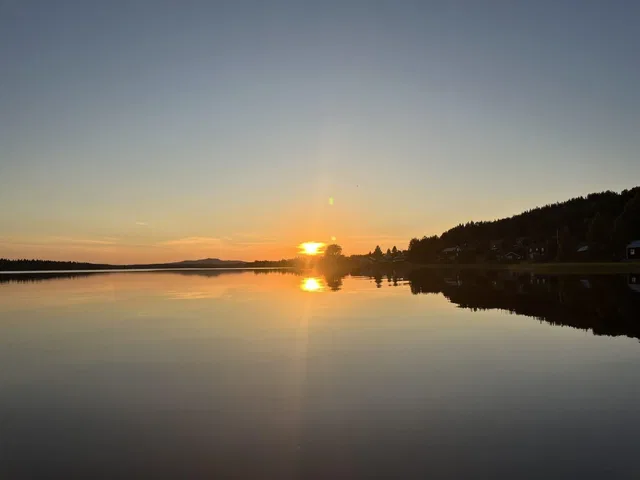 Sonnenuntergang über einem ruhigen See mit bewaldetem Ufer.