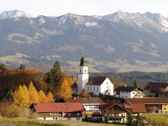 Alpen-Dorf mit Kirche und Bergen im Hintergrund