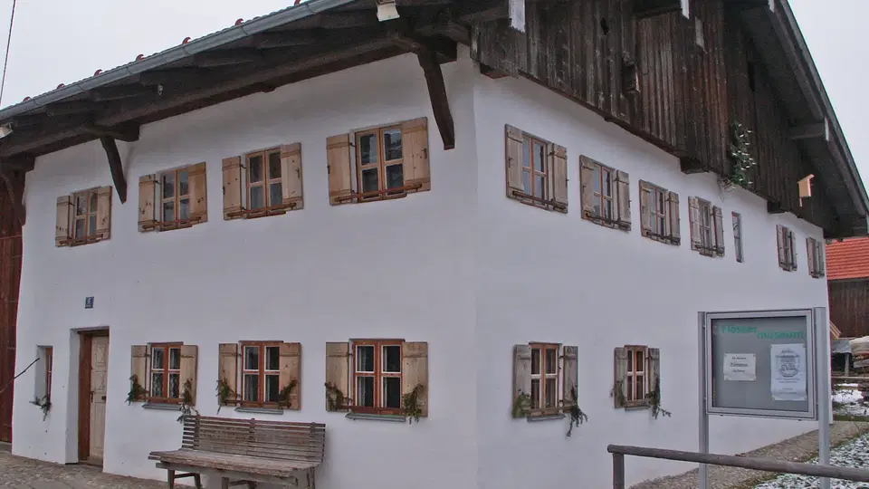 Weiße zweistöckige Fassade mit Holzfenstern und Bank davor