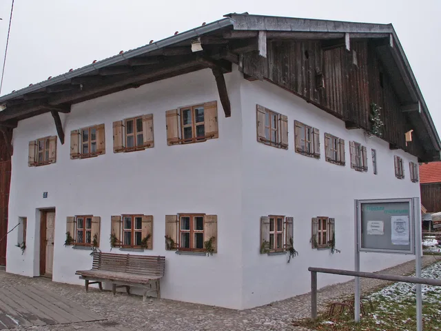 Weiße zweistöckige Fassade mit Holzfenstern und Bank davor