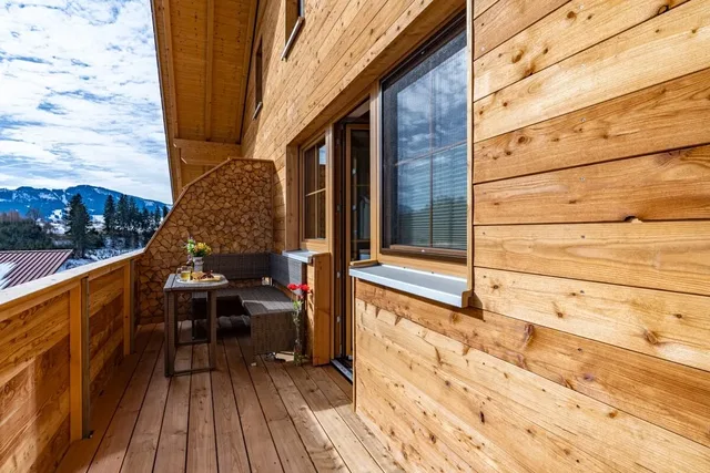 Holzterrasse am Chalet mit Sitzgelegenheiten und Kaminholz, Berglandschaft im Hintergrund.