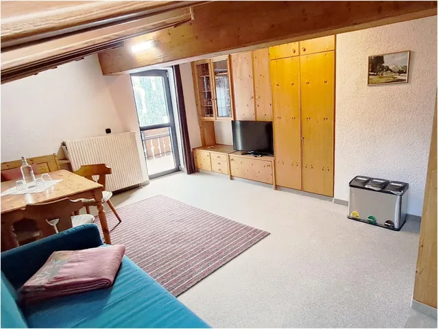 Wohnzimmer im Dachgeschoss mit Holzmöbeln, TV, Sofa und Teppich.