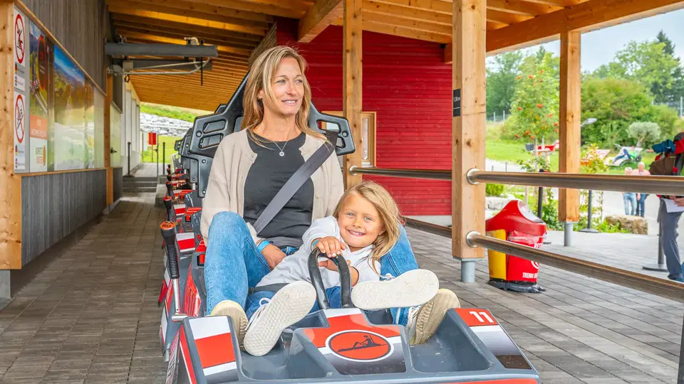 Frau und Kind im AlpspitzCOASTER-Fahrzeug am Einstieg