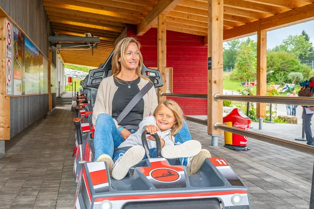 Frau und Kind im AlpspitzCOASTER-Fahrzeug am Einstieg