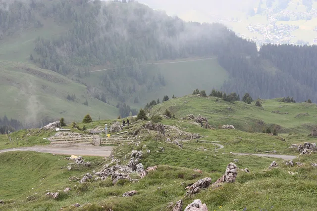 Landschaft mit grasbewachsenen Hängen, Felsen und Wanderweg, Nebel im Hintergrund