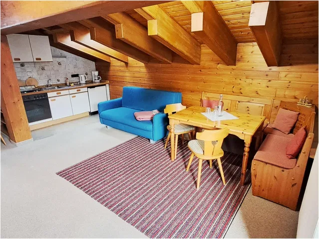 Gemütliches Dachgeschoss mit Holzbalken, Küche, blauem Sofa und Esstisch im Wohnbereich.