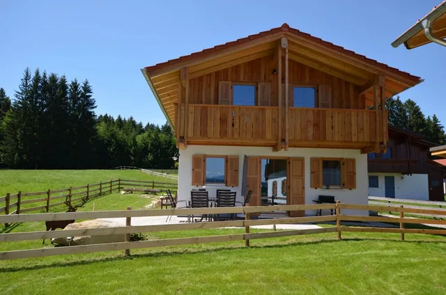 Holzhaus mit Balkon an einer Wiese vor einem Wald