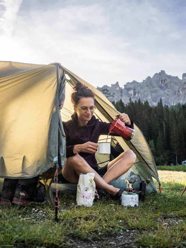 Frau gießt Kaffee vor dem gelben Zelt auf einem Campingplatz