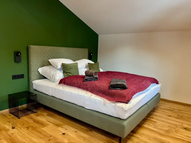 Modernes Schlafzimmer mit grüner Wand, großem Bett und rotem Überwurf.