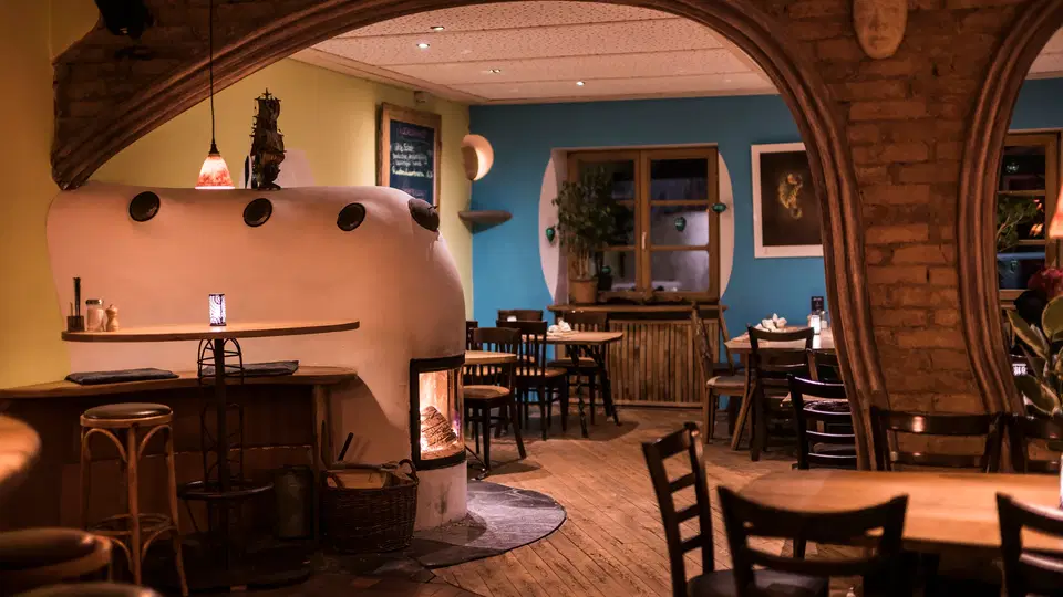 Gemütliches Restaurantinterieur mit Bogenarchitektur, Holztischen und einer weißen Backofenwand.