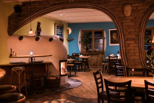Gemütliches Restaurantinterieur mit Bogenarchitektur, Holztischen und einer weißen Backofenwand.