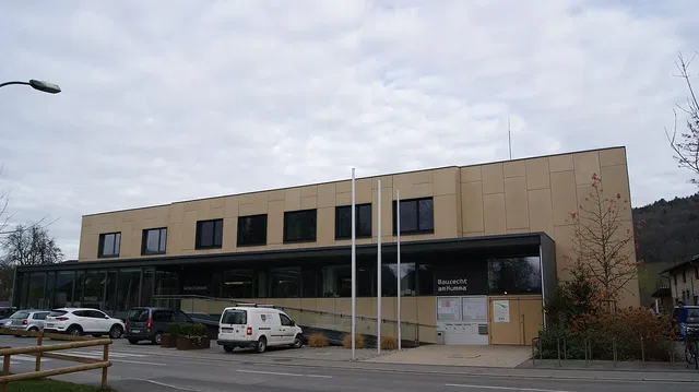 Modernes Verwaltungsgebäude mit Glasfront und Parkplatz vor dem Eingang.
