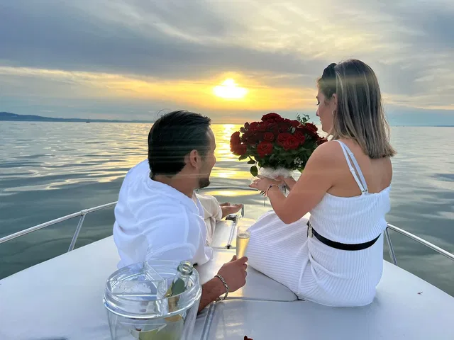 Paar auf Boot bei Sonnenuntergang, Frau mit Rosenstrauß, Mann mit Sekt