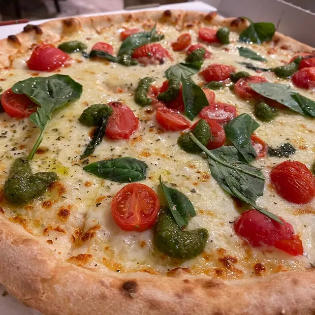Pizza mit Kirschtomaten, Basilikumblättern und Pesto auf knusprigem Rand.