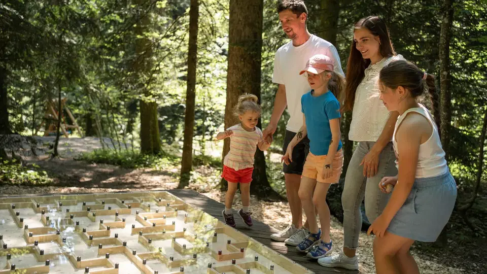 Familie spielt im Wald an einem großen Holzlabyrinth