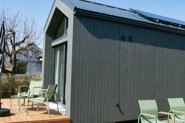 Außenansicht eines modernen dunklen Holzhauses mit Sonnendeck und Gartenmöbeln