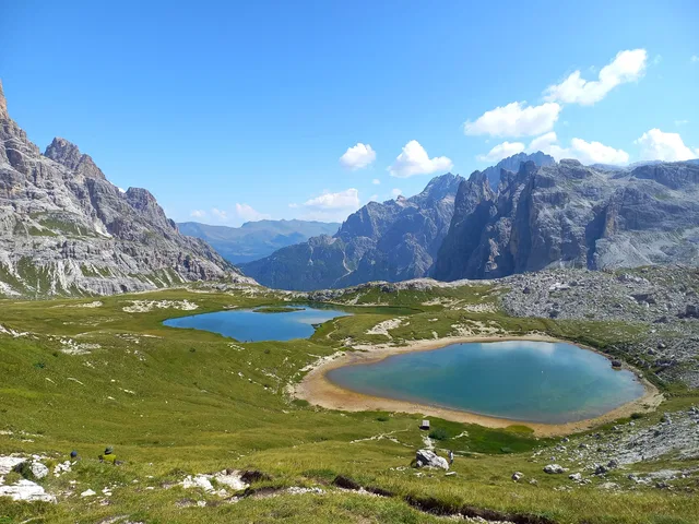 Zwei Bergseen zwischen grünen Wiesen und felsigen Gipfeln.