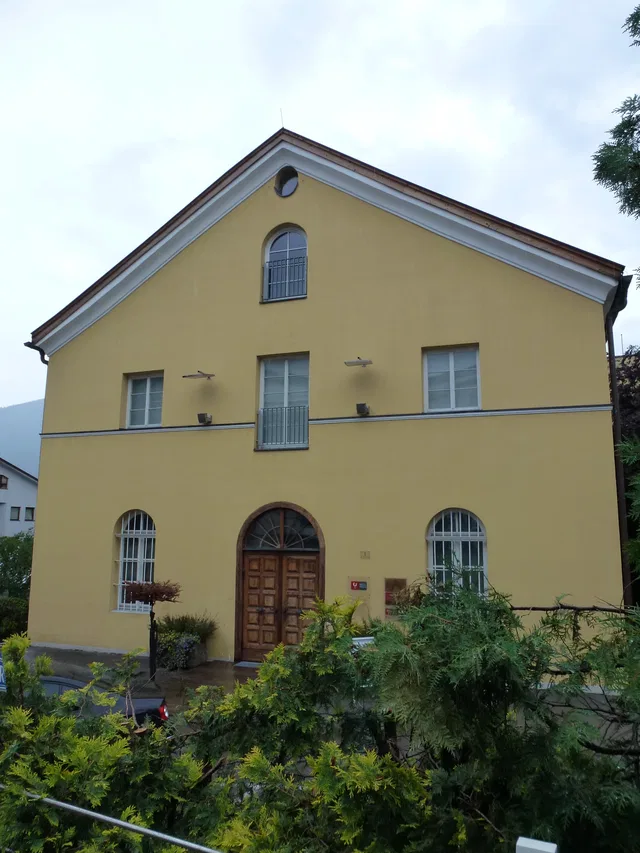 Gelb gestrichene zweigeschossige Villa mit Rundbogenfenstern, Holztür und kleinem Vorgarten.
