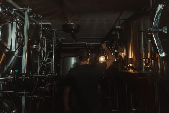 Mann bedient große Metallanlage in dunkler Dampfbierbrauerei