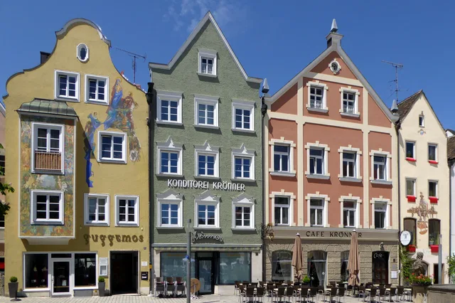 Bunte Häuserzeile mit Café-Terrassen und Terrassenbestuhlung unter blauem Himmel.