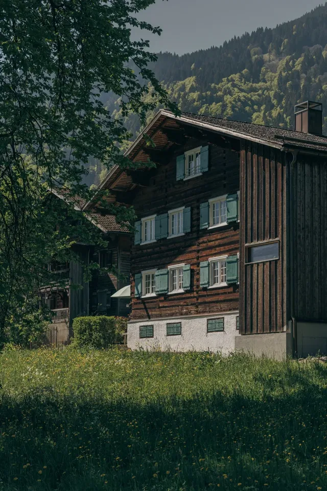 Holz-Chalet mit grünen Fensterläden vor Wald- und Berglandschaft.
