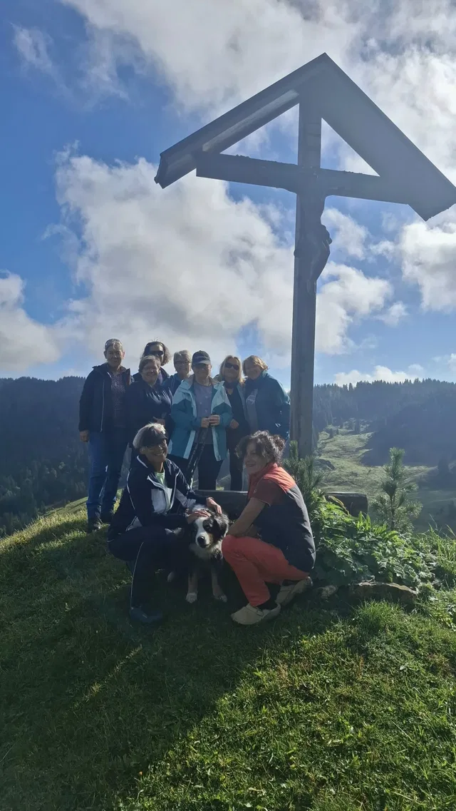Wandergruppe mit Hund an einem Gipfelkreuz.