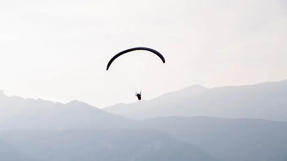 Dunkler Gleitschirm vor mehreren blass im Dunst liegenden Bergketten.