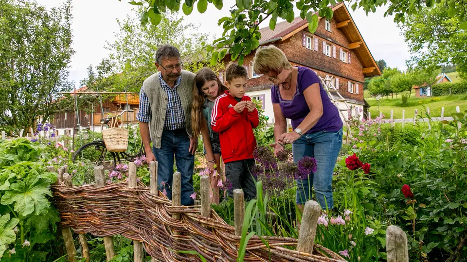 Familie im Garten vor Holzhaus mit Weidenzaun und Blumen