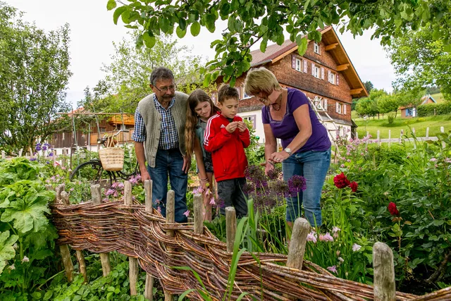 Familie im Garten vor Holzhaus mit Weidenzaun und Blumen