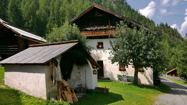 Alpines Bauernhaus mit Holzbalustrade, weißer Fassade, Garten und Baum davor