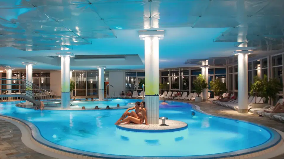 Indoor-Pool mit Insel im Zentrum, umlaufende Säulen und Liegebereich.