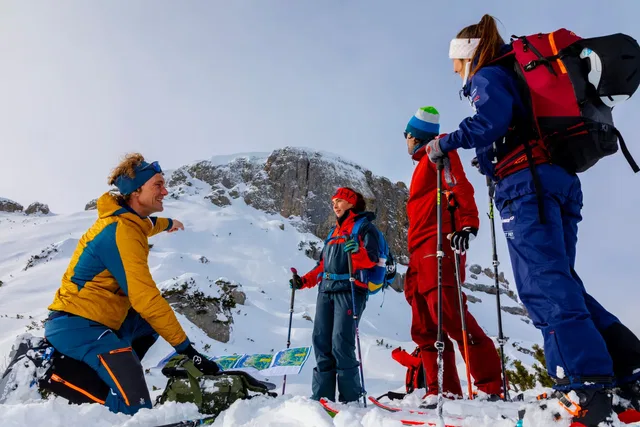 Vier Bergsteiger im Winteroutfit beraten sich über eine Karte auf einem verschneiten Gipfel