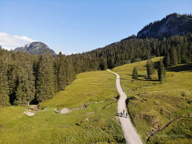 Radfahrende auf einem Schotterweg durch Bergwiesen