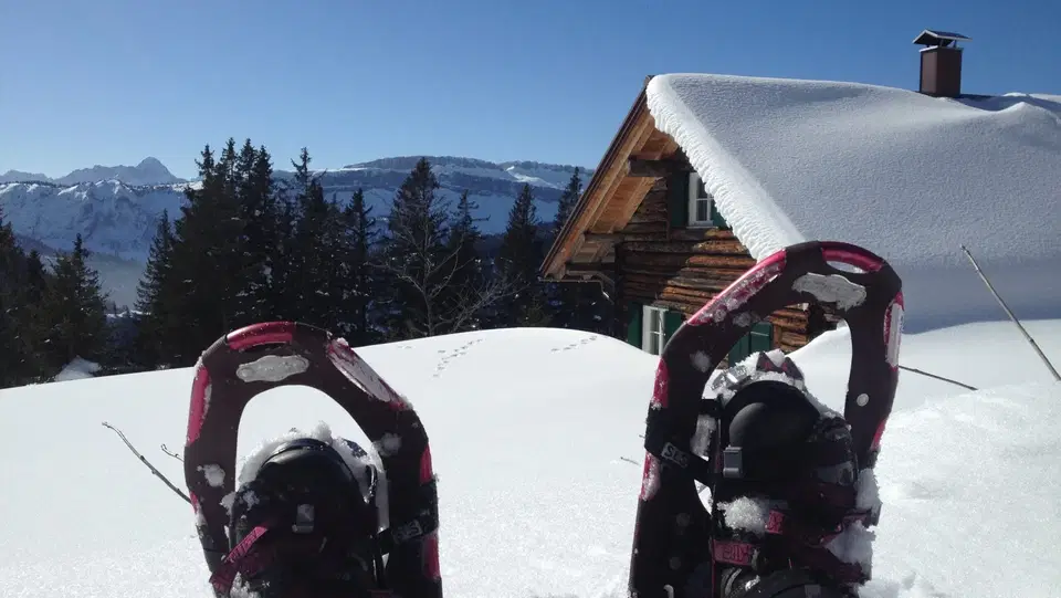 Schneeschuhe an den Füßen vor einer eingeschneiten Holzhütte