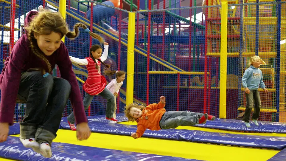 Junge und Mädchen springen in einer Trampolinanlage in einem farbenfrohen Innenpark.