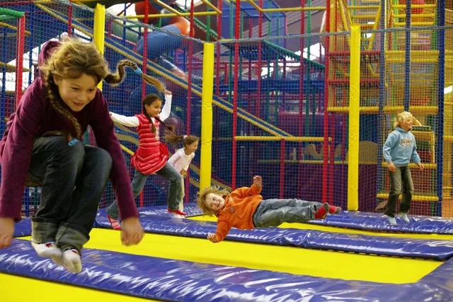 Junge und Mädchen springen in einer Trampolinanlage in einem farbenfrohen Innenpark.