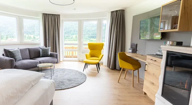 Offener Wohnbereich mit Fensterfront, grauem Sofa, gelbem Sessel, Arbeitstisch und Kamin.