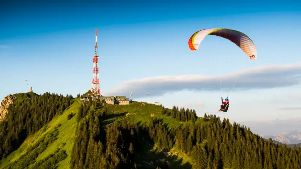 Paragleiter fliegt über grüne Bergkuppe mit Sendemast
