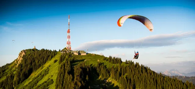 Paragleiter fliegt über grüne Bergkuppe mit Sendemast
