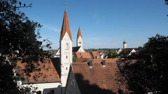 Dächer und schlanke Türme des Crescentiaklosters vor der Kaufbeurer Altstadt, von einem begrünten Hang aus gesehen. Ortsmotiv zur Ausflugsplanung.
