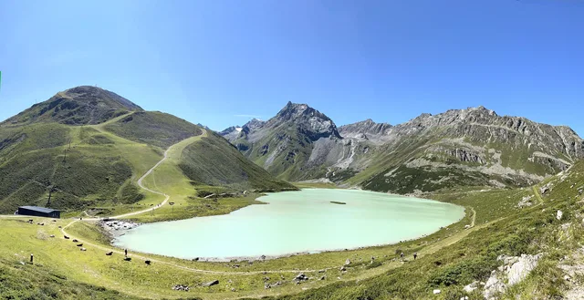 Türkisfarbener Bergsee in einer grünen Alpenlandschaft, umgeben von Bergen.