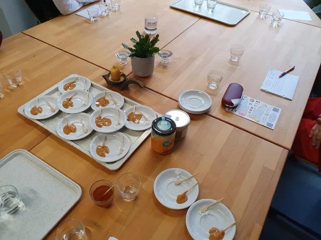 Tischrunde mit Dessertportionen auf Tellern, zentrale Pflanze, Gläser und Unterlagen.